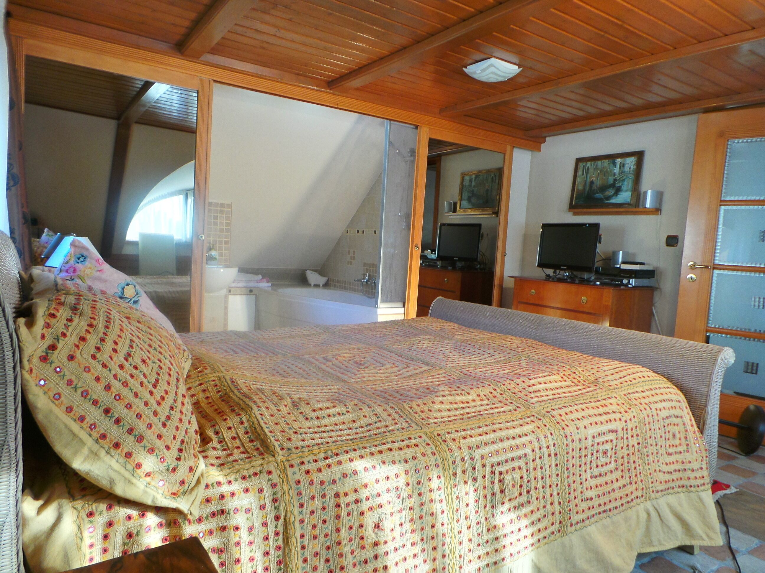 Ein Schlafzimmer mit einem großen Bett, einem Fernseher, einem Schreibtisch und einem durch eine offene Tür einsehbaren Badezimmer.