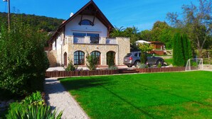 Une maison à deux étages avec une façade en pierre, un balcon et une allée menant à une voiture garée.