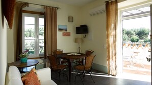 A dining area with a round table and chairs, a television mounted on the wall, and a window with curtains.