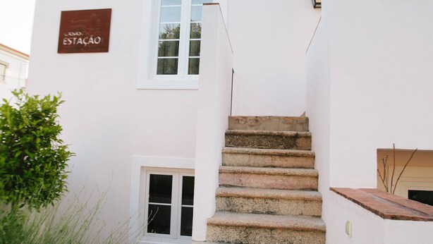 A white building with a sign reading "ESTACAO" and a set of stone steps leading to a door.