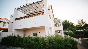 A modern two-story building with a white facade, a covered patio, and a stone wall in the foreground.