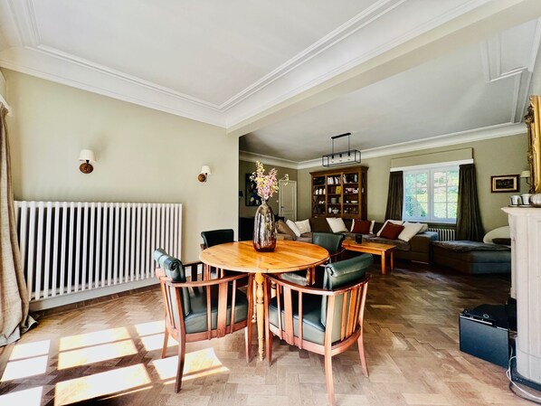 Un salón amplio con una mesa de comedor de madera, asientos cómodos, una estantería y vistas al exterior.