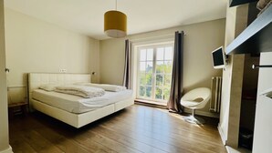 A bedroom with a bed, a bedside table, a chair, a TV, and a window with curtains.
