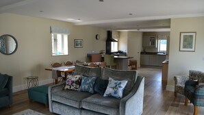 Ein Wohnzimmer mit grauem Sofa, einem Essbereich mit Tisch und Stühlen sowie einer Küche im Hintergrund.
