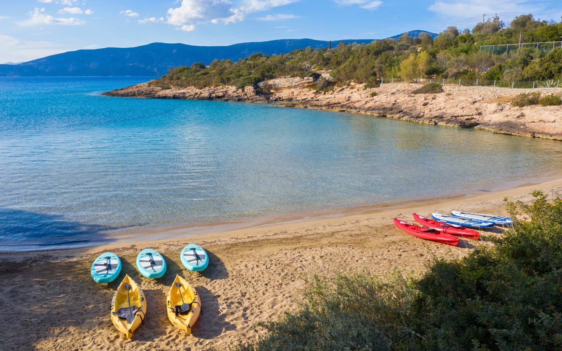 A beach with kayaks and a clear view of the sea and mountains in the background.