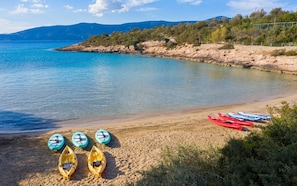Una playa con kayaks y una vista despejada del mar y montañas al fondo.