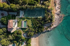 Vista aérea de una propiedad costera con cancha de tenis, piscina y acceso a la playa.