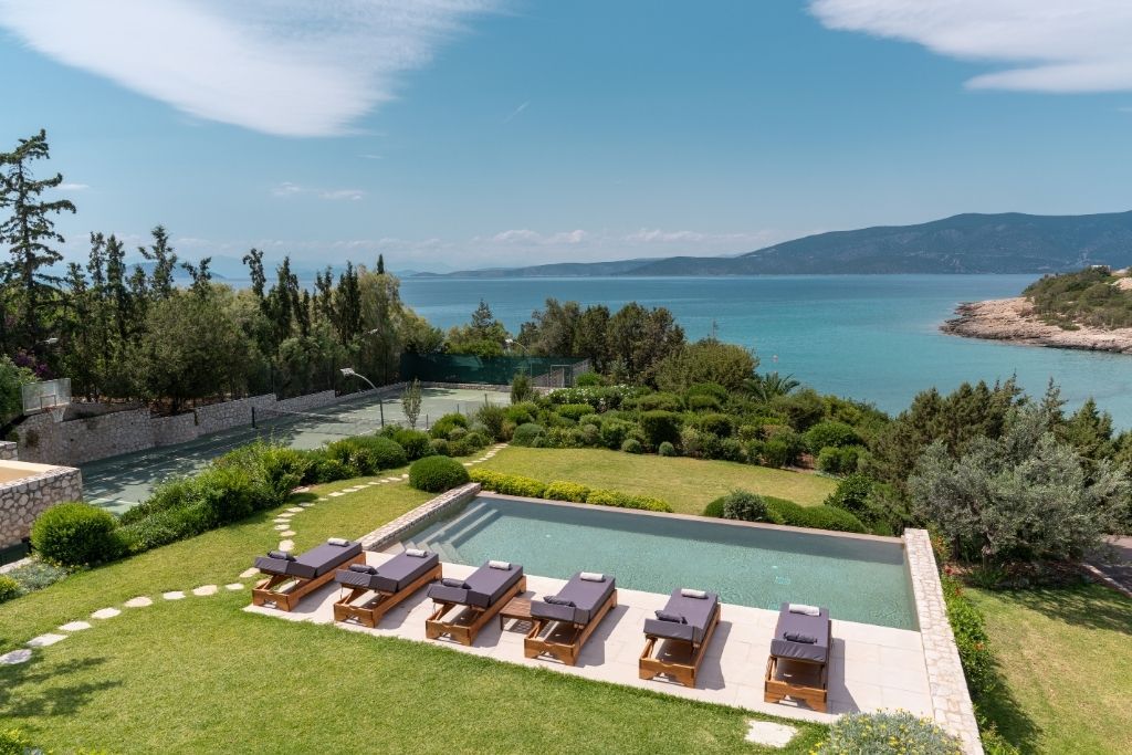 Une piscine entourée de chaises longues, elle-même bordée d’un jardin aménagé et offrant une vue sur la mer.