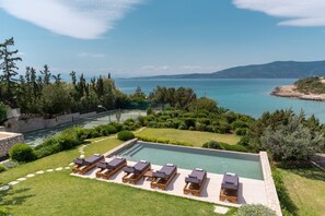 A swimming pool with lounge chairs, surrounded by a landscaped garden and a view of the sea.