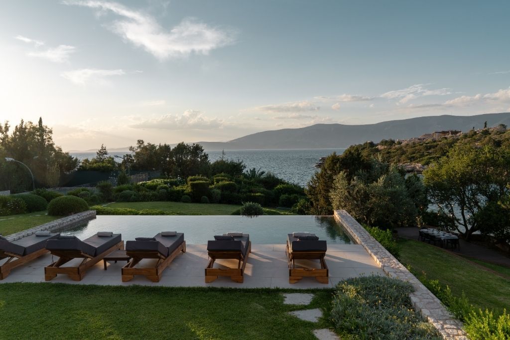 A pool area with lounge chairs, a view of the sea, and landscaped gardens.