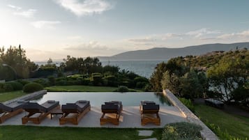 Ein Poolbereich mit Liegestühlen, Blick auf das Meer und angelegten Gärten.