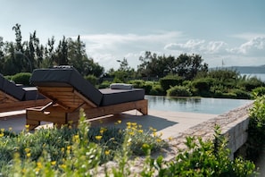 Zona junto a la piscina con sillas de descanso y vista al agua.