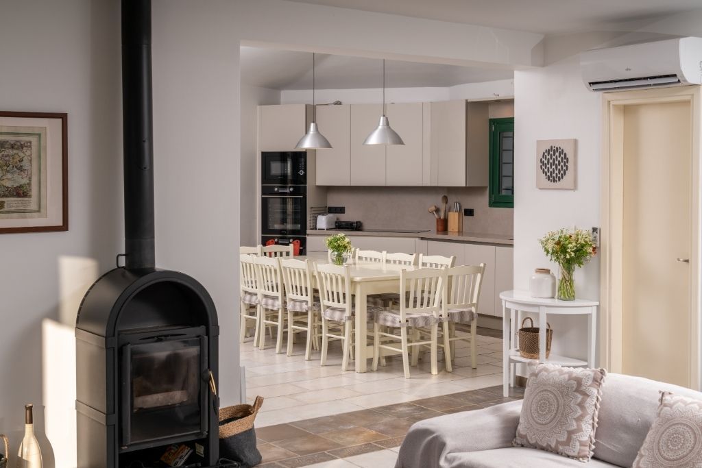 A modern living room with a fireplace, a dining area with chairs, and a kitchen in the background.