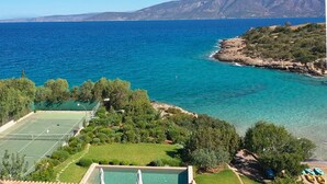 Uma propriedade costeira com quadra de tênis, vegetação exuberante e vista para o mar e montanhas.