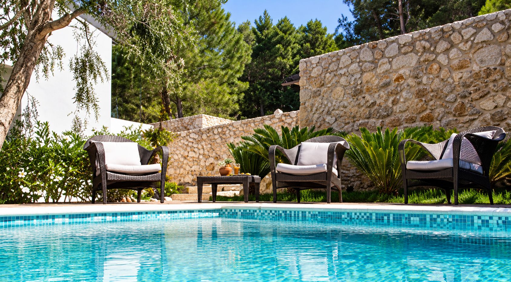 A swimming pool with lounge chairs and a stone wall.