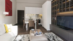A modern living room with a sofa, a coffee table with magazines, a TV, and a kitchen in the background. - The One Kensington (London)