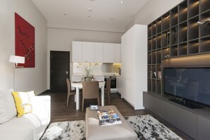 A modern living room with a sofa, a coffee table with magazines, a TV, and a kitchen in the background.