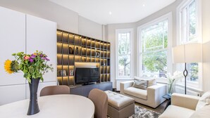 A modern living room with a dining area, a television, and a bookshelf. - The One Kensington (London)