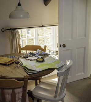 Une table à manger avec une carte, un verre à vin et des papiers, une chaise blanche et une fenêtre donnant sur des bâtiments en pierre.