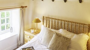 Camera da letto con testiera in legno, lampadario, comodino con lampada e finestra con tende.