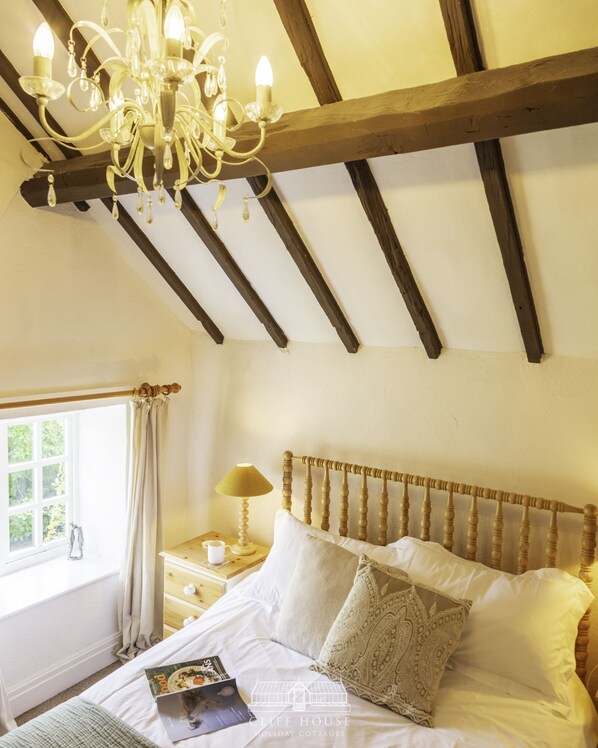 Une chambre à coucher avec une tête de lit en bois, un lustre, une table de chevet avec une lampe et une fenêtre avec des rideaux.