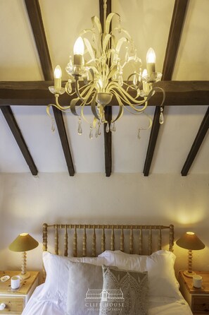 Une chambre à coucher avec un lustre, une tête de lit en bois, deux tables de chevet avec des lampes et un lit avec des oreillers.