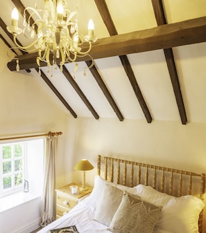 A bedroom with a wooden headboard, a chandelier, a bedside table with a lamp, and a window with curtains.