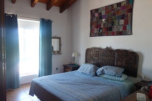 Un dormitorio con una cama grande, un cabecero con intrincados grabados, un tapiz acolchado y una ventana con cortinas.
