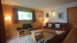 Un salon chaleureux avec des murs en bois, un canapé, une table basse, un téléviseur et une lampe.