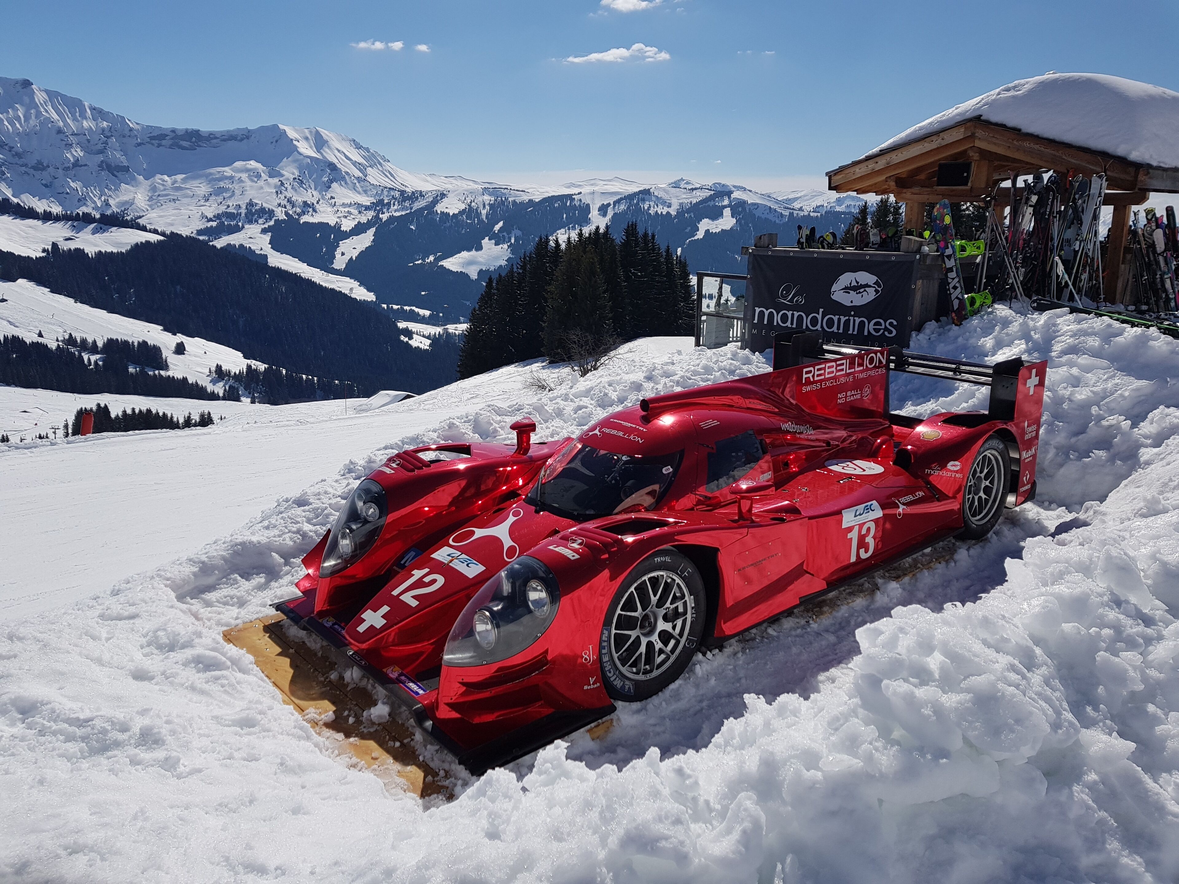 Un coche deportivo rojo aparcado en la nieve, con montañas al fondo.