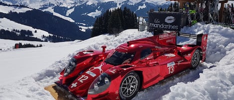 Une voiture de sport rouge est garée dans la neige, avec une chaîne de montagnes en arrière-plan.