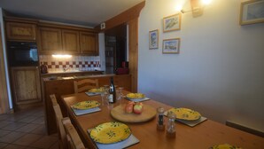 Une cuisine avec des meubles en bois, une table à manger pour quatre personnes et un mur recouvert de carreaux.