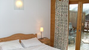 Une chambre avec une tête de lit en bois, une lampe de chevet et une vue sur une terrasse extérieure avec des chaises.