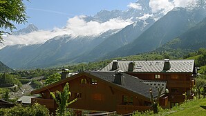 Un chalet en bois, doté d’un toit à pente, entouré d’une végétation luxuriante et avec des montagnes en toile de fond.