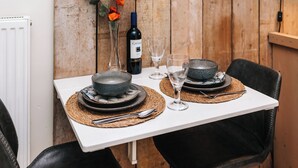 Mesa posta com pratos, tigelas e uma garrafa de vinho, com parede de madeira rústica ao fundo.