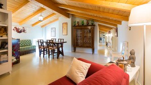 Amplia sala de estar con techo de madera, una mesa de comedor con sillas, un sofá rojo y un aparador con objetos decorativos.