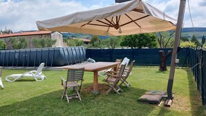 Un patio trasero con una mesa y sillas de madera, una piscina inflable blanca y un paraguas grande.