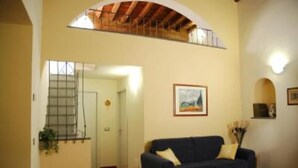 A living room with a blue sofa, a painting on the wall, and a staircase leading to an upper level. - apartment in Santa Croce 52 in Florence ( Italy) (Firenze)