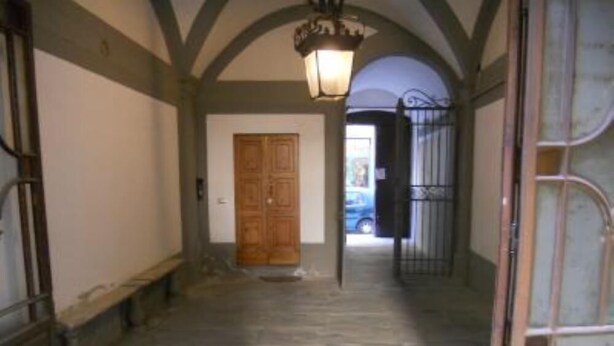A hallway with a wooden door, a metal gate, and a stone floor. - apartment in Santa Croce 52 in Florence ( Italy) (Firenze)