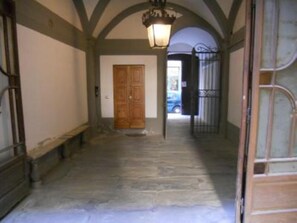 A hallway with a wooden door, a metal gate, and a stone floor. - apartment in Santa Croce 52 in Florence ( Italy) (Firenze)