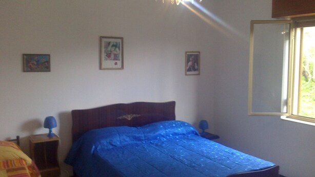 A bedroom with a bed, a nightstand, a lamp, and a window.