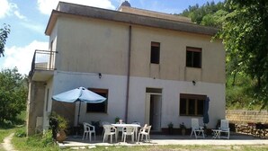 Un bâtiment à deux étages doté d’un balcon, d’un espace extérieur aménagé avec des chaises et une table, et d’un grand parasol.