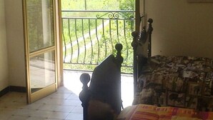 Une chambre à coucher comprenant un lit, une table de chevet, une fenêtre donnant sur un paysage verdoyant et un ventilateur de plafond.