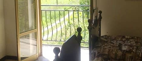 A bedroom with a bed, a nightstand, a window with a view of a green landscape, and a ceiling fan.
