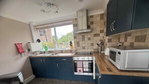 A compact kitchen with dark blue cabinets, a built-in oven, a microwave, and a window providing a view of the outdoors.
