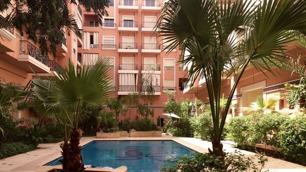 A courtyard with a swimming pool surrounded by planters and palm trees. - City center, air-conditioned apartment in secure residence with swimming pool. (Marrakech)