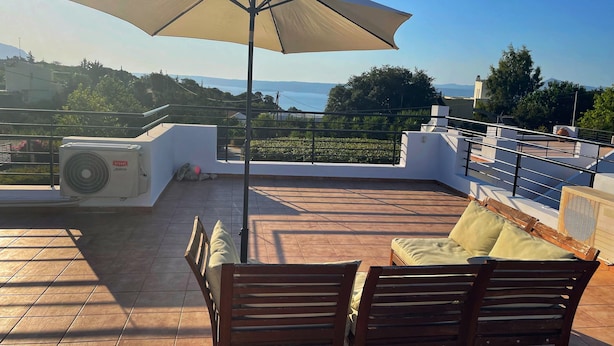 A rooftop terrace with a table and chairs, an umbrella, and a view of the sea.