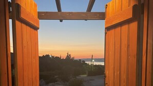 An open wooden door leading to a balcony with a table and chairs, overlooking a scenic view.