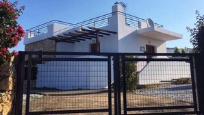 A modern two-story house with a white exterior, a balcony, and a gated driveway.