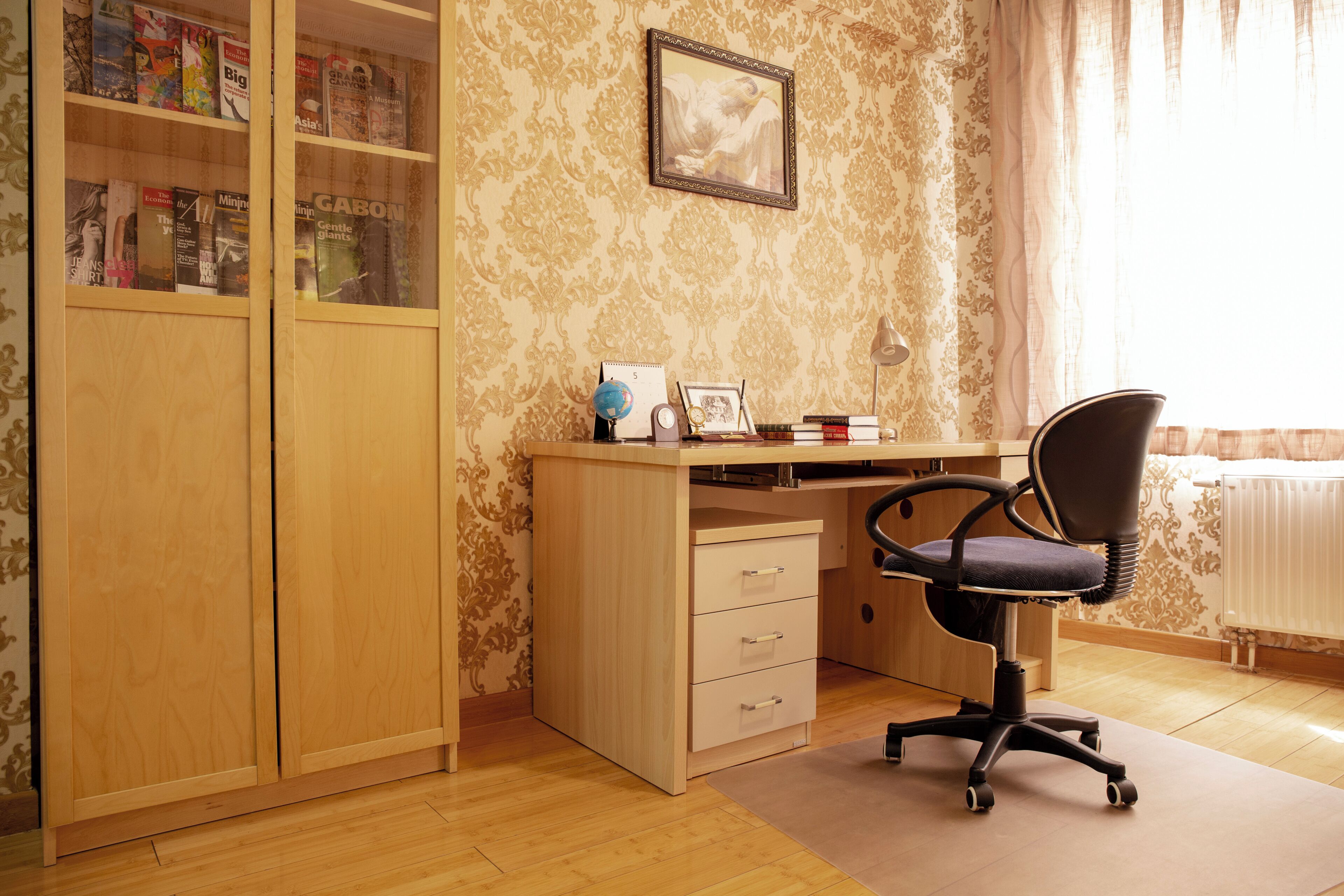 A study room with a wooden desk, a chair, a bookshelf, and a framed picture on the wall.